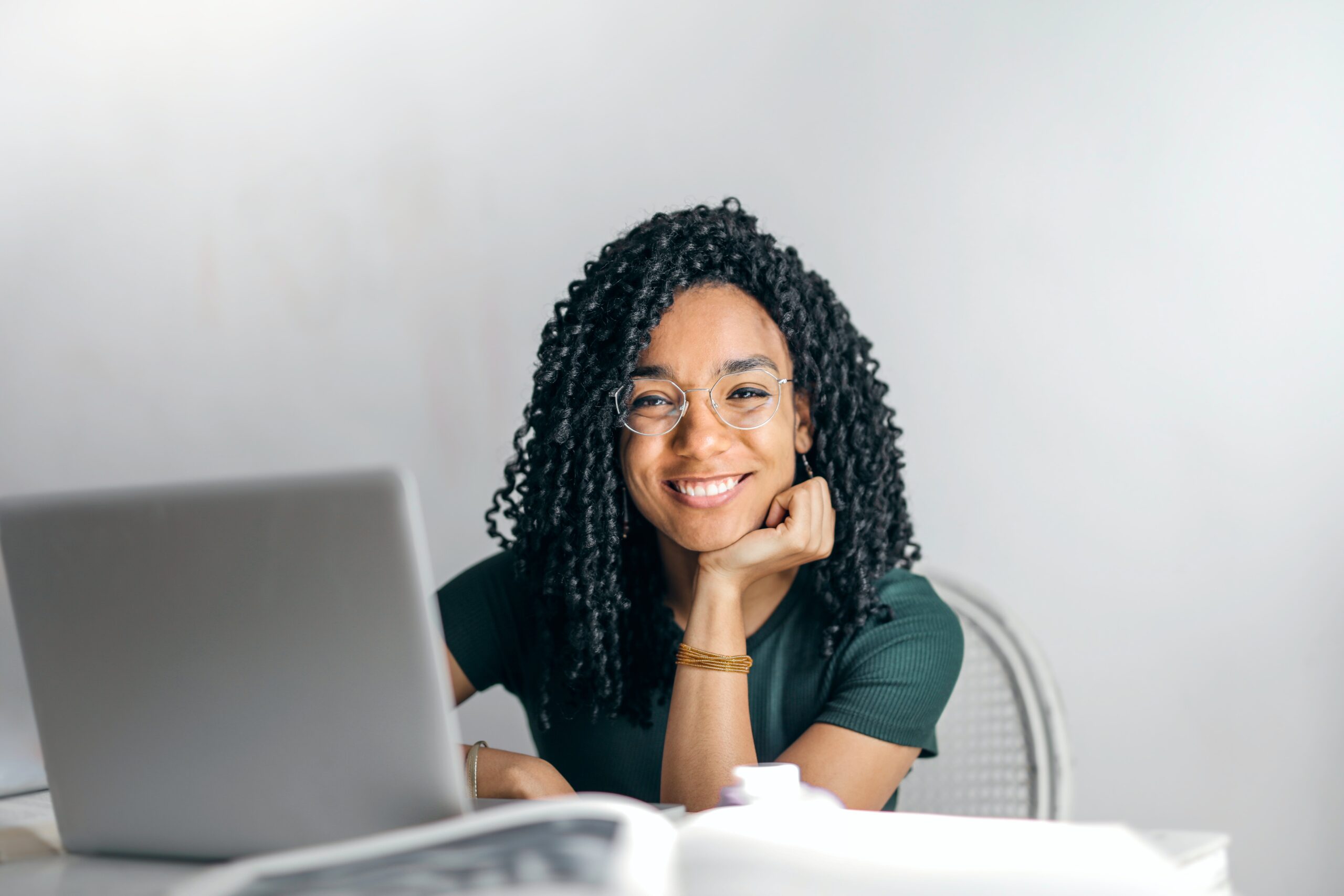 Woman sitting at a desk smiles from behind a laptop